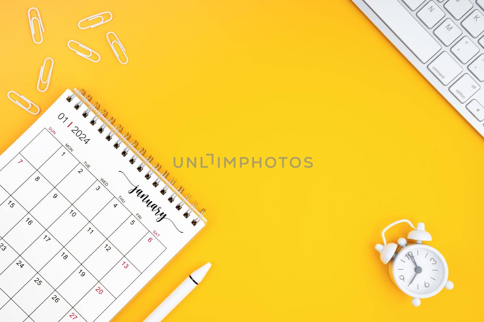 January 2024, Monthly desk calendar for 2024 year and alarm clock with paper clips on yellow color background.  by Gamjai