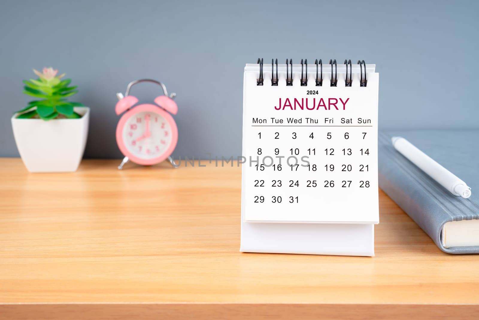 January Monthly desk calendar for 2024 year and alarm clock on wooden table.