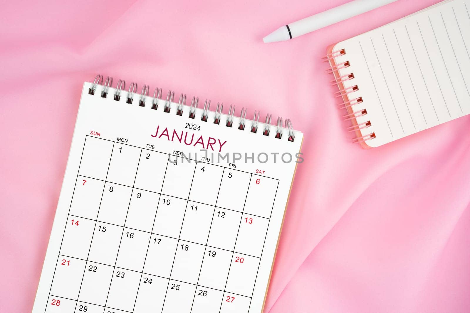 January 2024 month calendar and pen with open diary on pink fabric background. Monthly calendar concept.