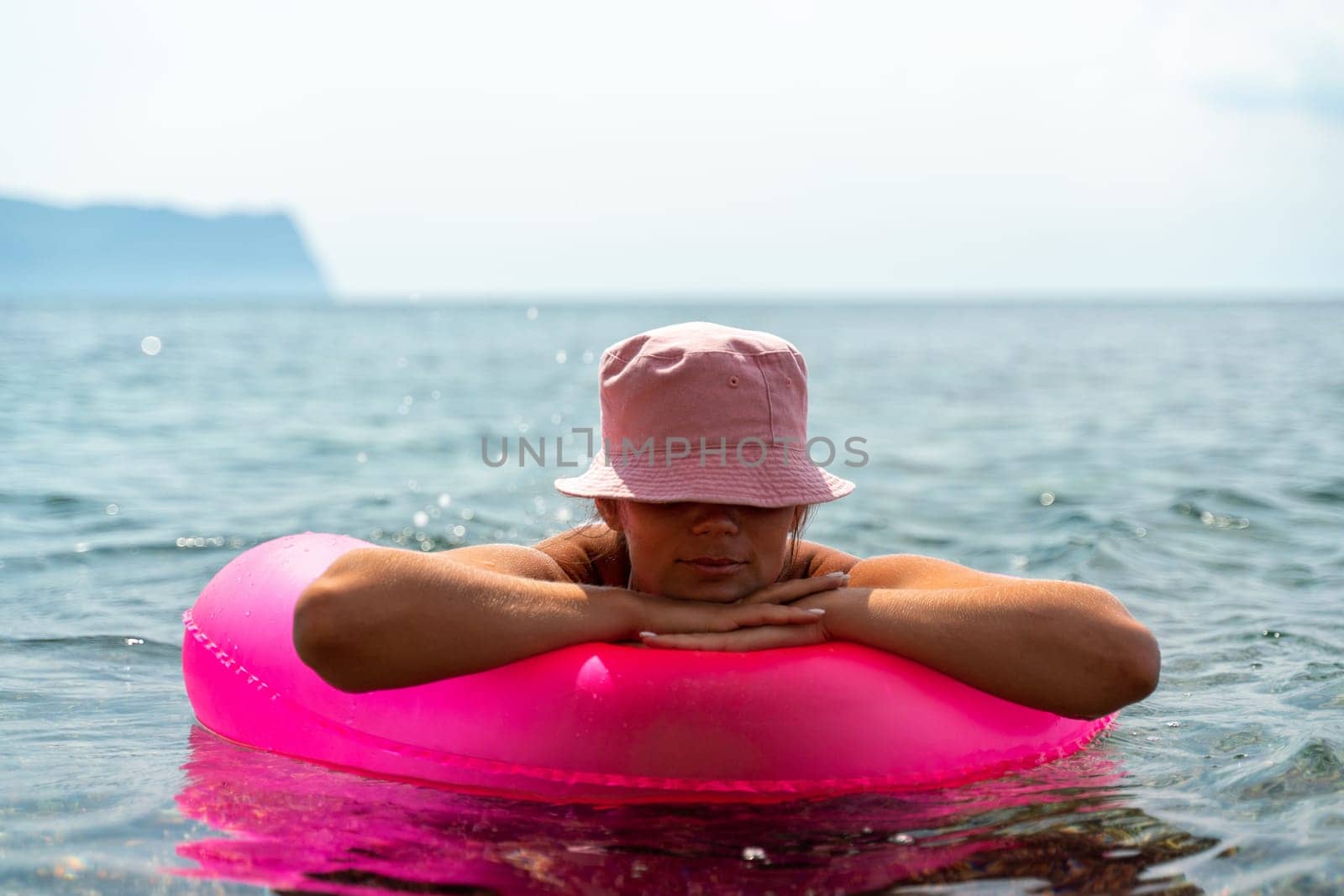 Summer vacation woman in hat floats on an inflatable donut mattress. Happy woman relaxing and enjoying summer travel holidays travel on the sea