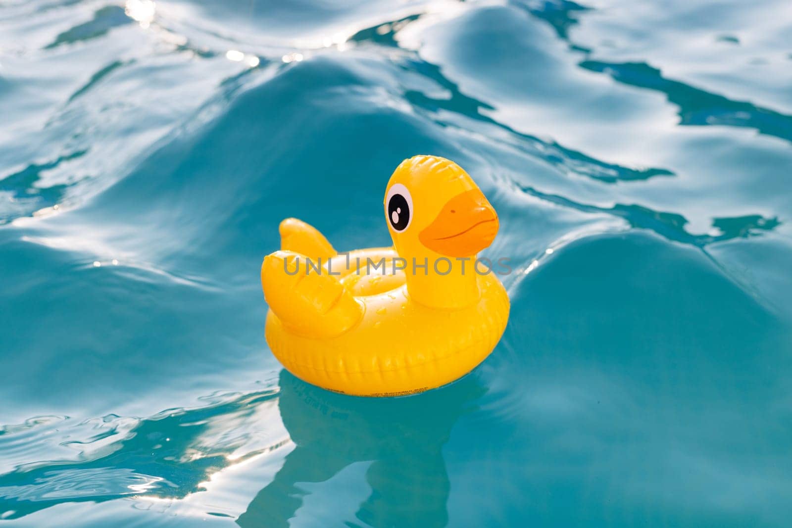Yellow inflatable duck floating on blue water in a pool on a hot summer day by andreyz