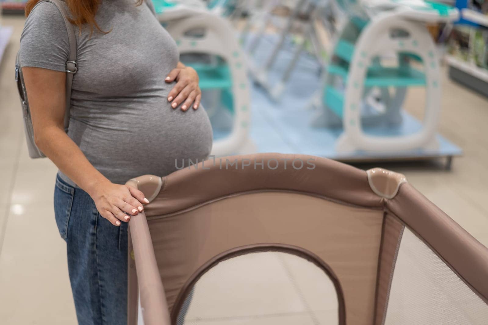 Caucasian pregnant woman chooses a playpen crib in a children's store