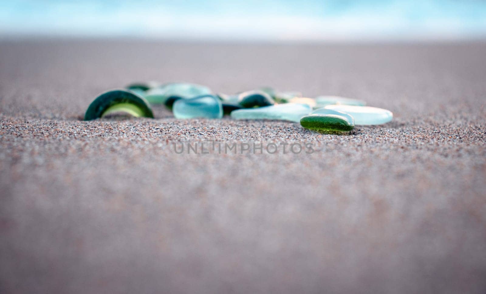 Sand beach and glass stones concept photo. Glass stones from broken bottles polished by the sea. Front view photography with blurred background. High quality picture for wallpaper, travel blog