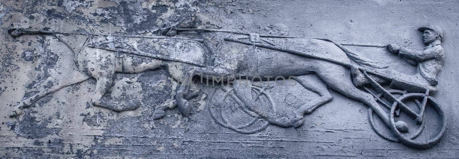 Close up metal relief with jockey and horses concept photo. Metal panel with ornament and horse rider figure. Part of antique old door photography. High quality picture