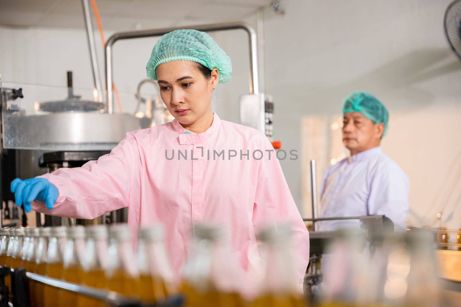 In a drink factory QC engineers examine glass bottles of fruit juice production. They wear protective gear ensuring top quality and hygiene in the manufacturing process.