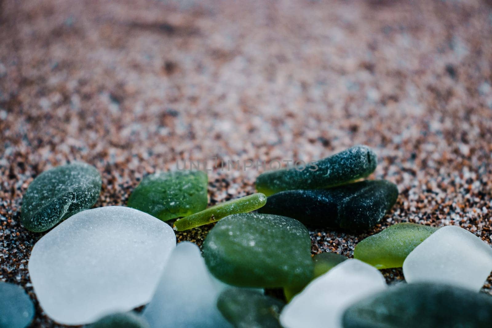 Sand beach and glass stones concept photo. Glass stones from broken bottles polished by the sea. Front view photography with blurred background. High quality picture for wallpaper, travel blog