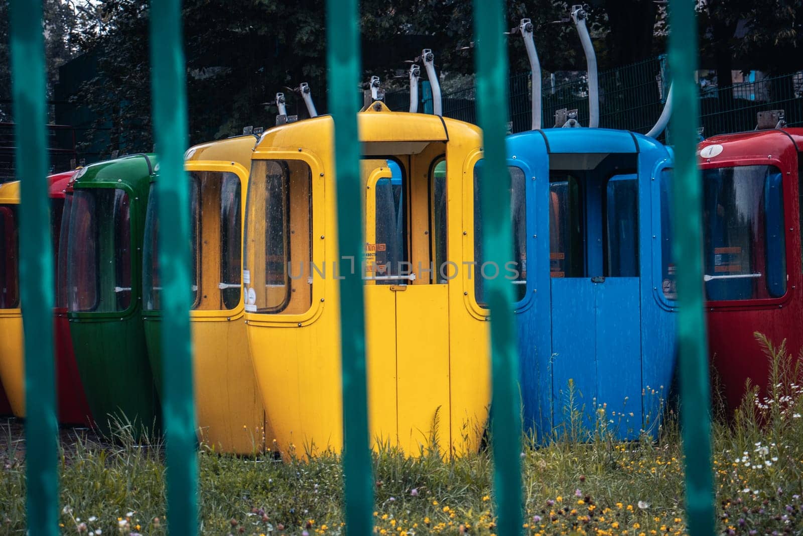Abandoned colorful funicular vehicle behind fence concept photo. Street scene, parkland. Cableway for transporting people in amusement park. High quality picture for wallpaper, travel blog.
