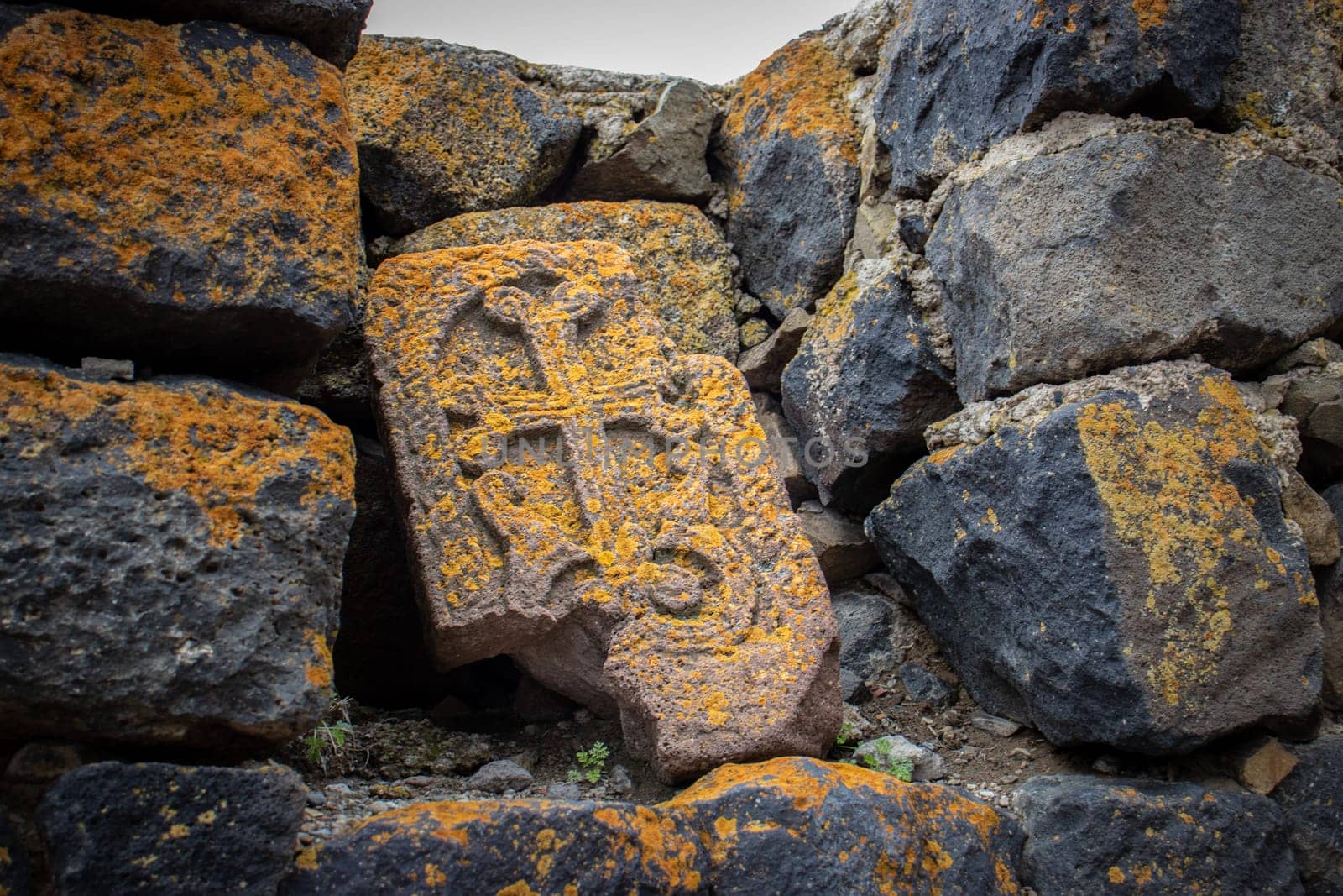 Close up stone cross with yellow lichen on rough stone wall concept photo. Historical tombs and head stones. Rocks full of the moss texture in nature for wallpaper.