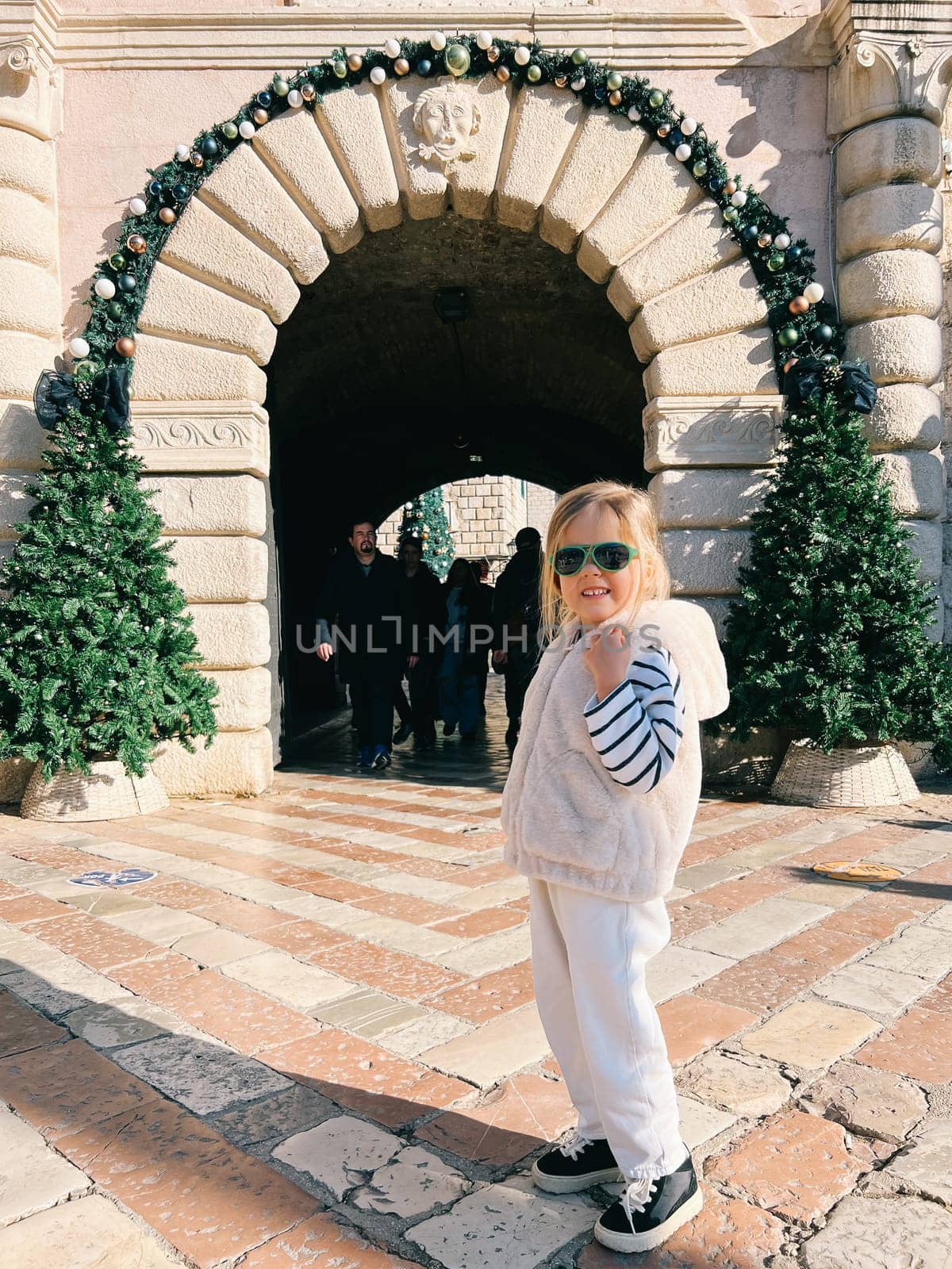 Little girl poses near the arch of an ancient building decorated with New Year garlands. High quality photo
