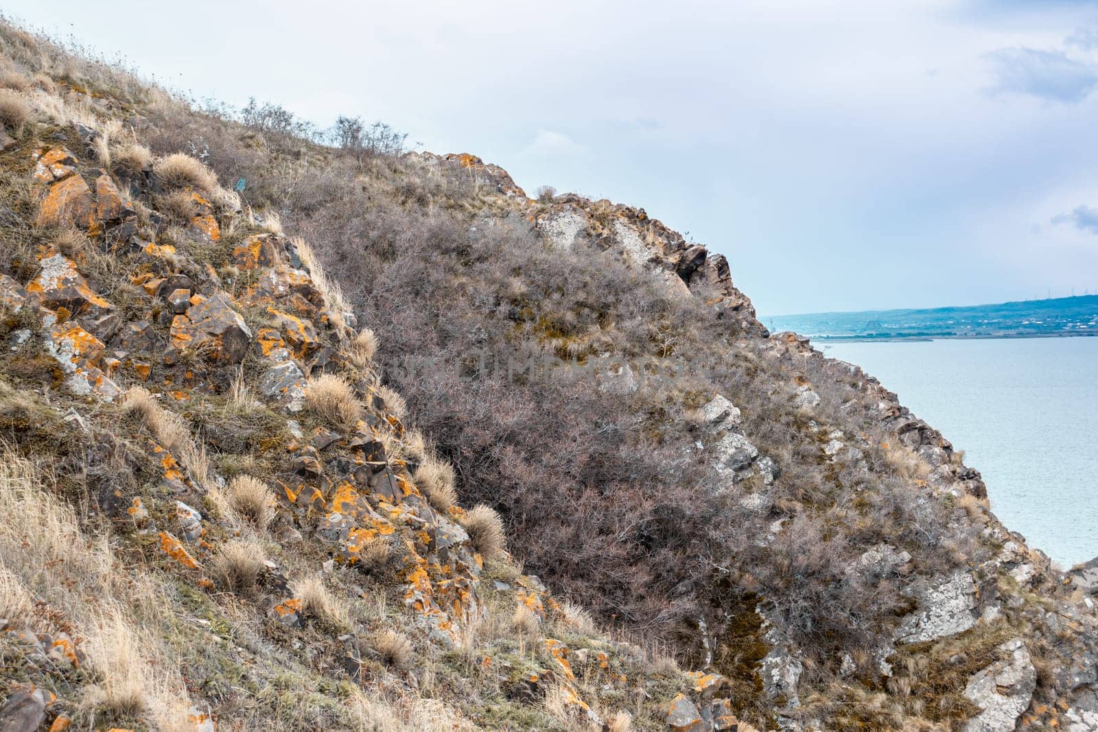 Hill view with rough stones and dry grass concept photo. Dramatic stormy sky and lake. High quality picture for wallpaper