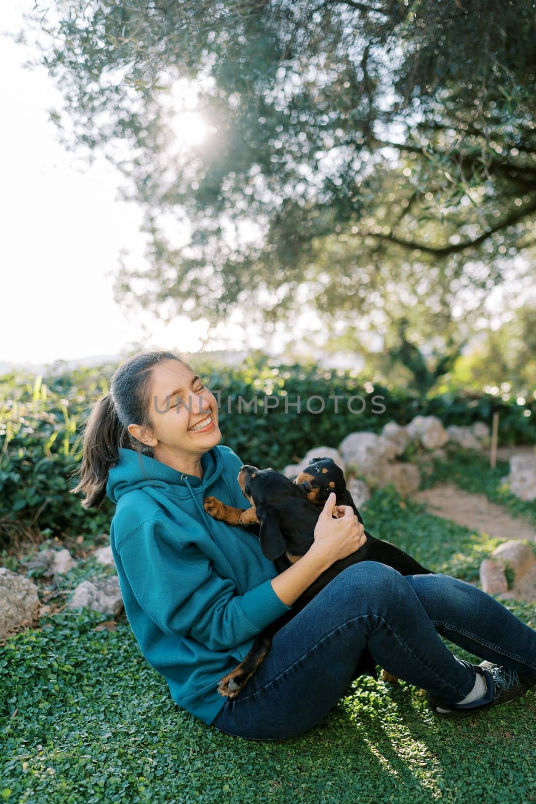 Young laughing woman holding puppies climbing in her face by Nadtochiy