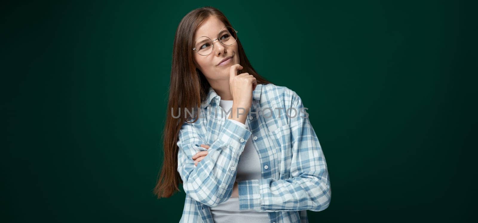 Charming young woman with brown hair thinking on a green background with copy space.