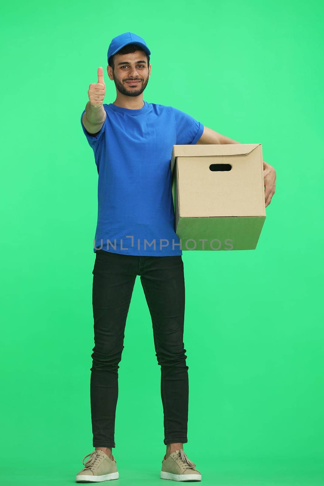 A man on a green background with box. Shows thumbs up sign.
