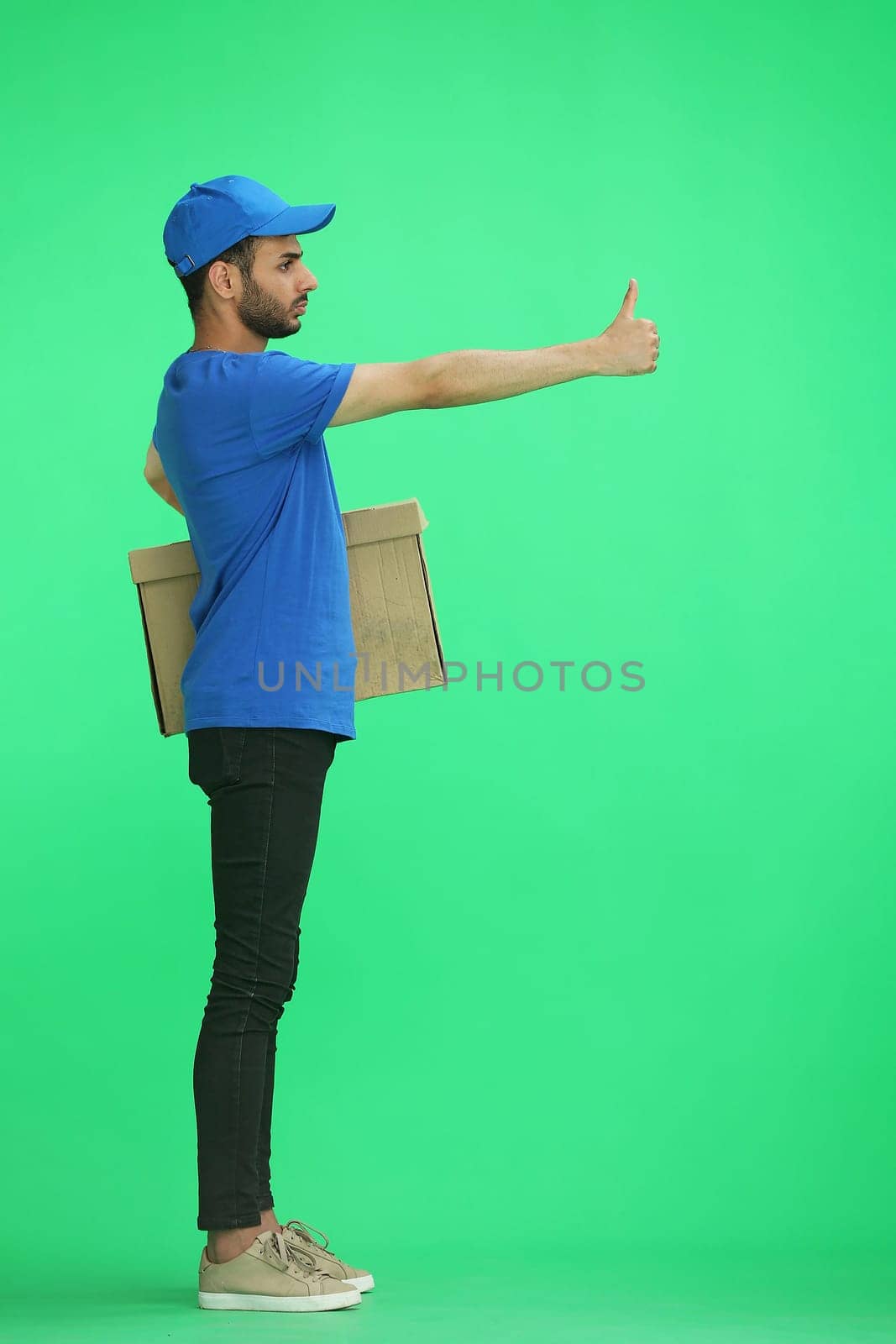 A man on a green background with box. Shows thumbs up sign, in profile.
