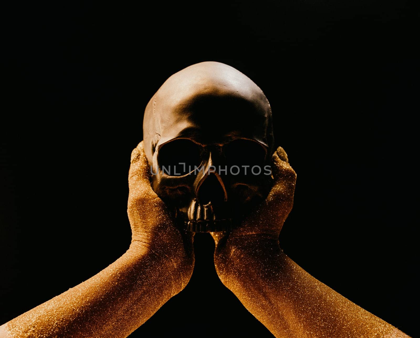 Golden female hand with human skull on black background. Mystique, ancient history concept. Power of symbolism - mortality and rebellion. Exploring life, death, gothic aesthetics. Dramatic metaphor.