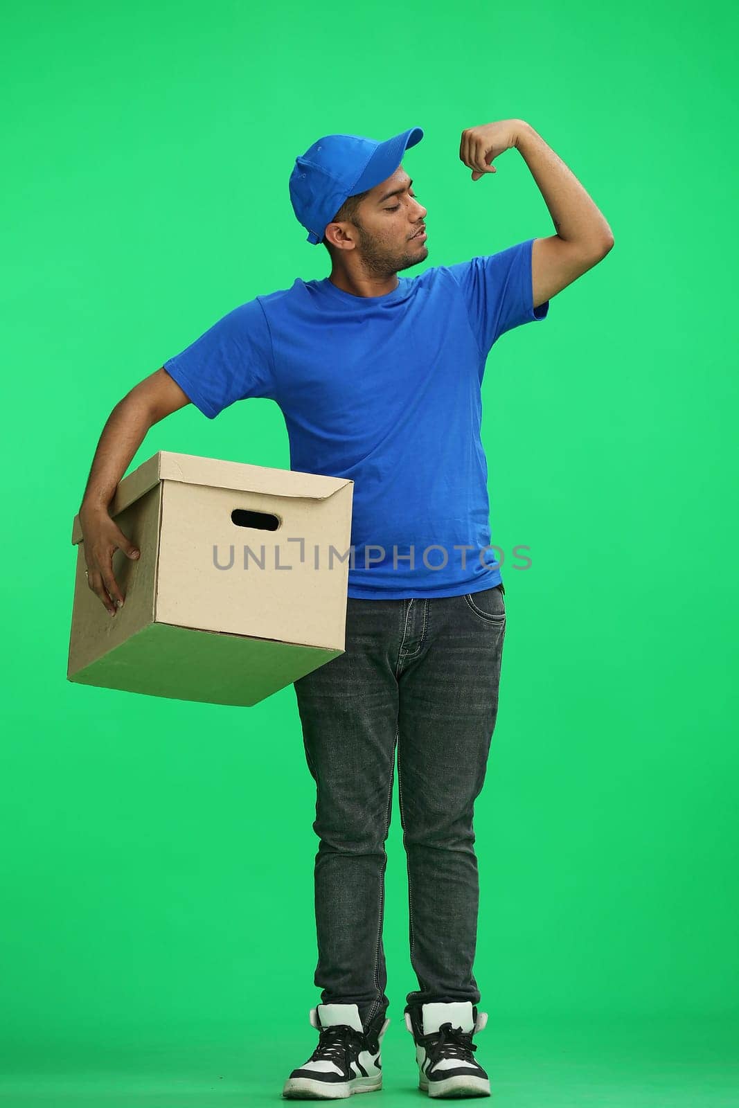 A man on a green background with box demonstrates strength with his hand.