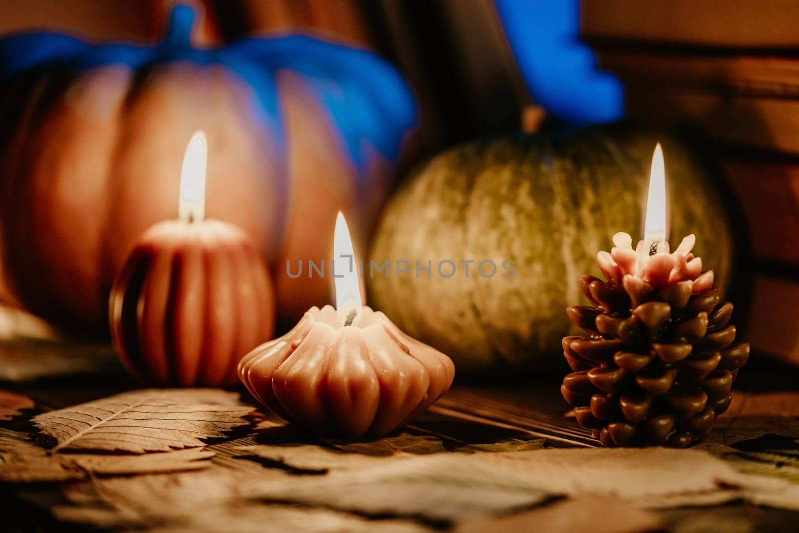 Autumn background. Pumpkin candle, orange fallen leaves. Flat lay. Cozy ambiance of fall, candle burning. Seasonal promotions or tranquil visual storytelling.