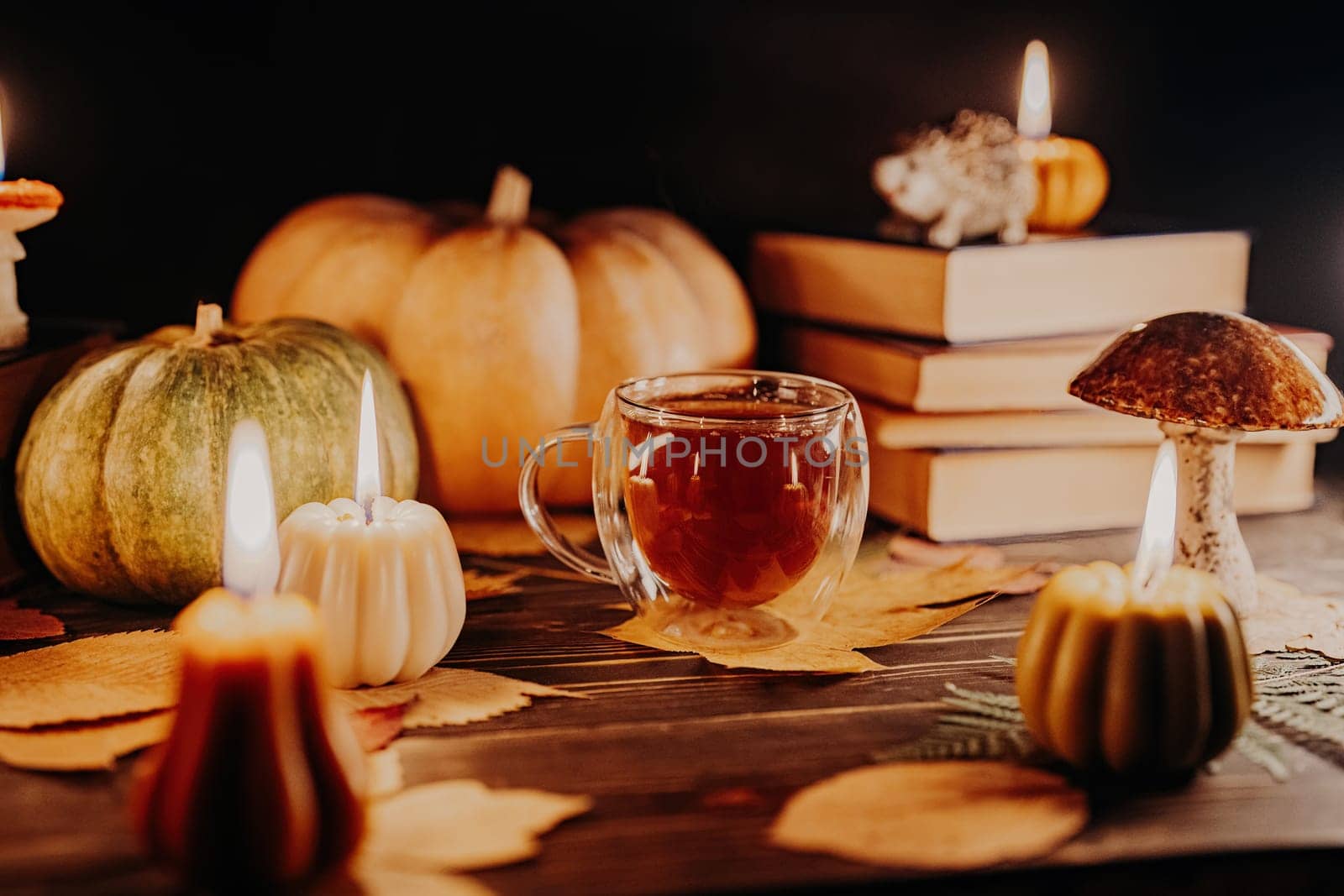 Glass cup of tea among pumpkin candles. Autumn-themed content, cafe promotions by kristina_kokhanova