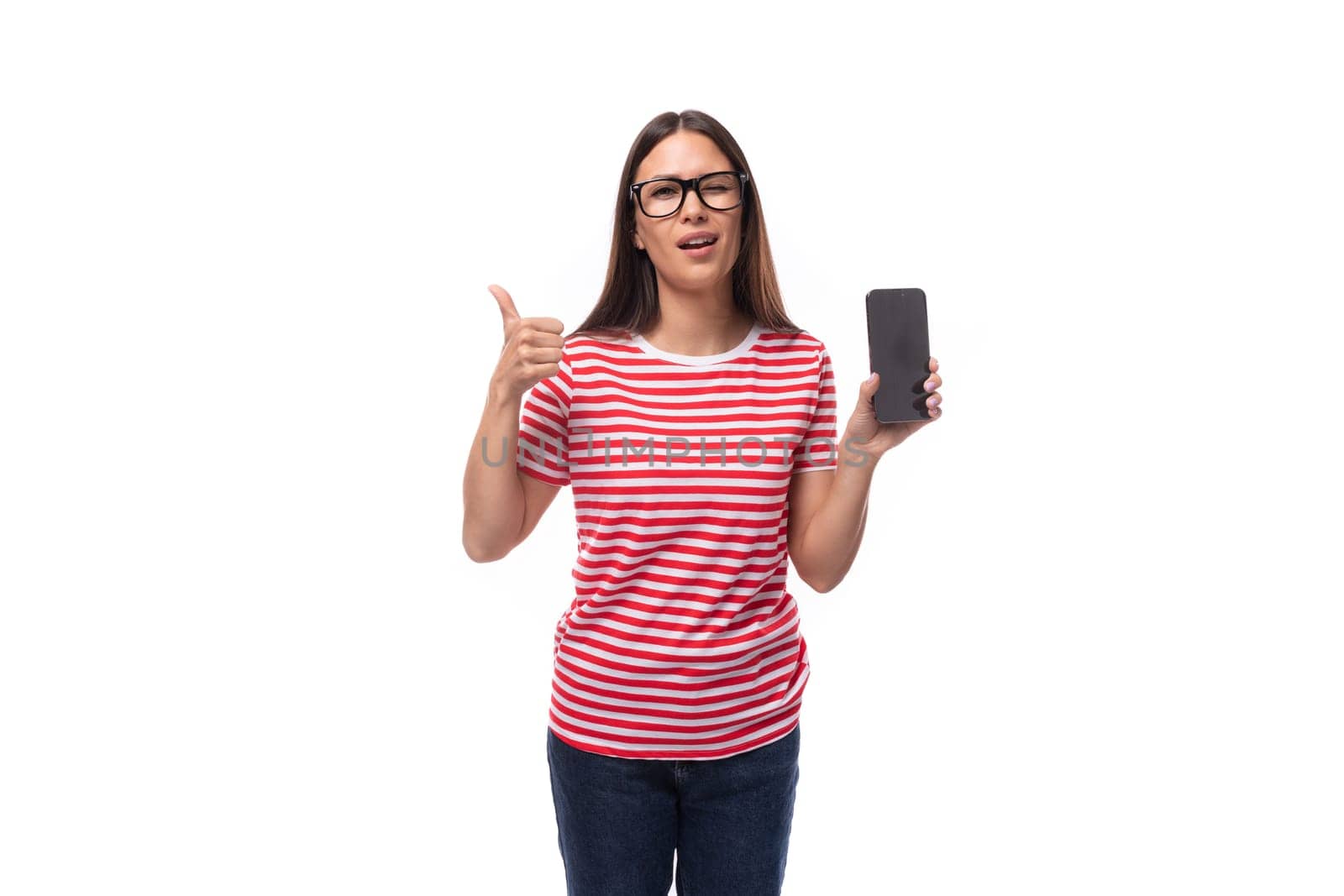 successful pretty 35 year old european lady in eyeglasses and a red striped t-shirt shows a mobile phone screen and a gesture of approval.