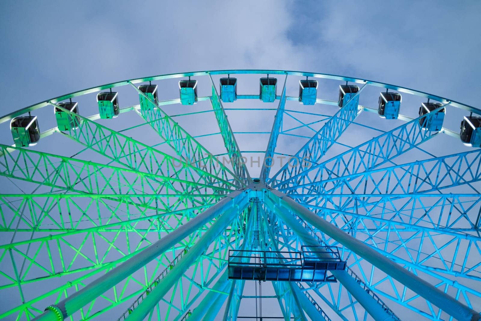 Underside view of colorful ferris wheel over evening sky at amusement park. High quality photo