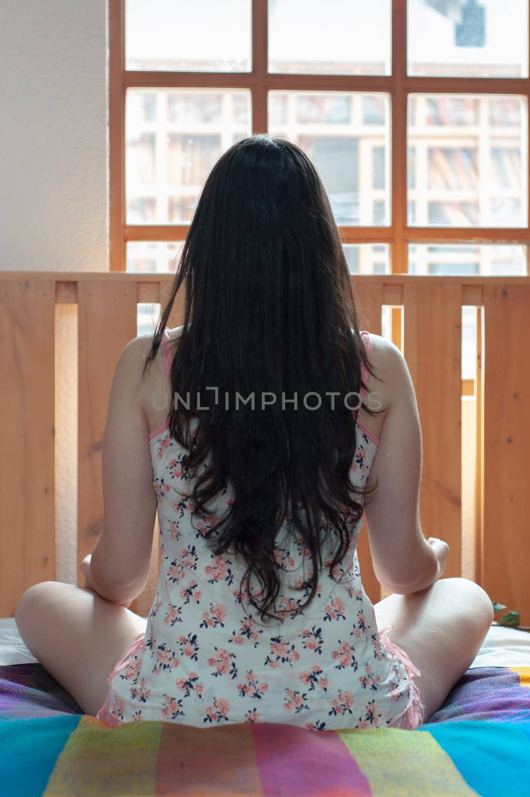 girl sitting on her bed looking at the light from the window doing relaxation exercises and finding her inner peace with her hair loose. yoga day. High quality photo