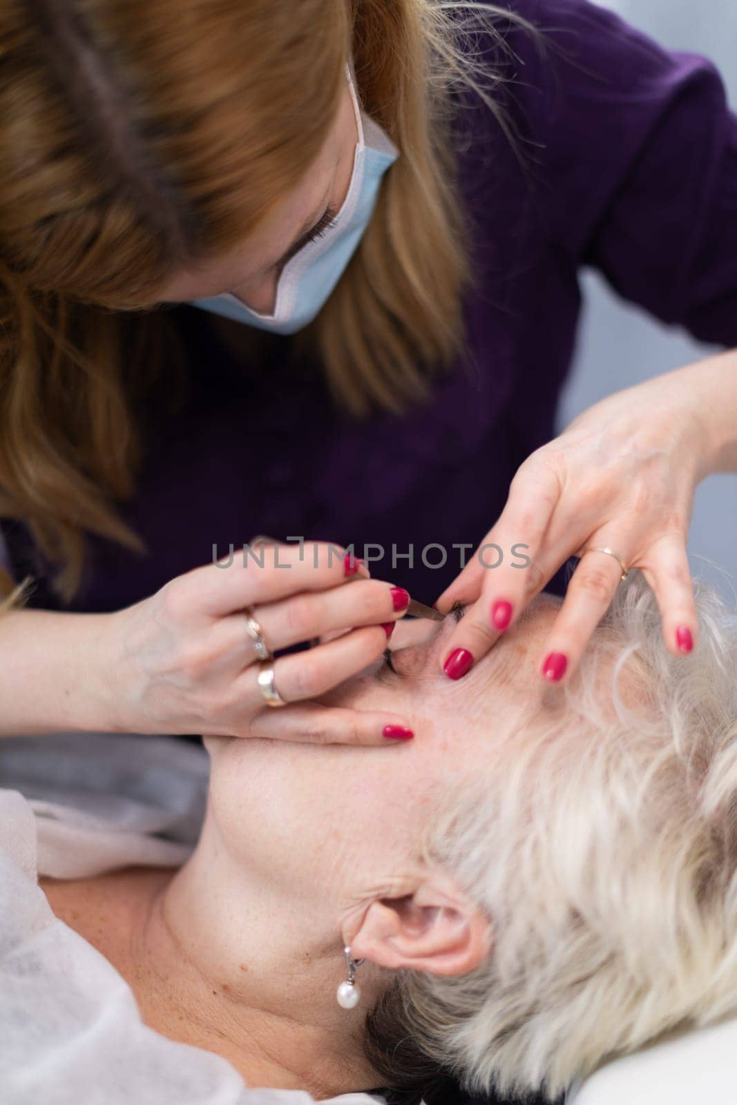 Close-up of the face of an elderly person lying on a bed. The beautician obscures the client's face with her hands while performing the treatment.