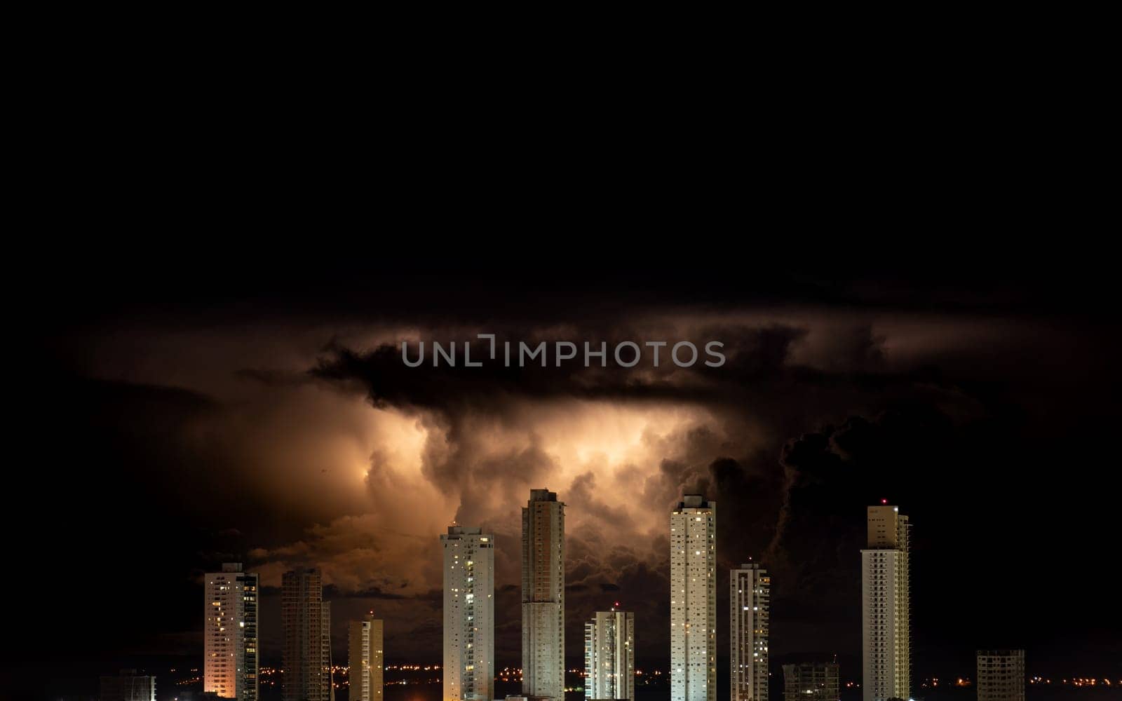 Massive skyscrapers form a barrier against the orange fire-like storm in the dark night sky.