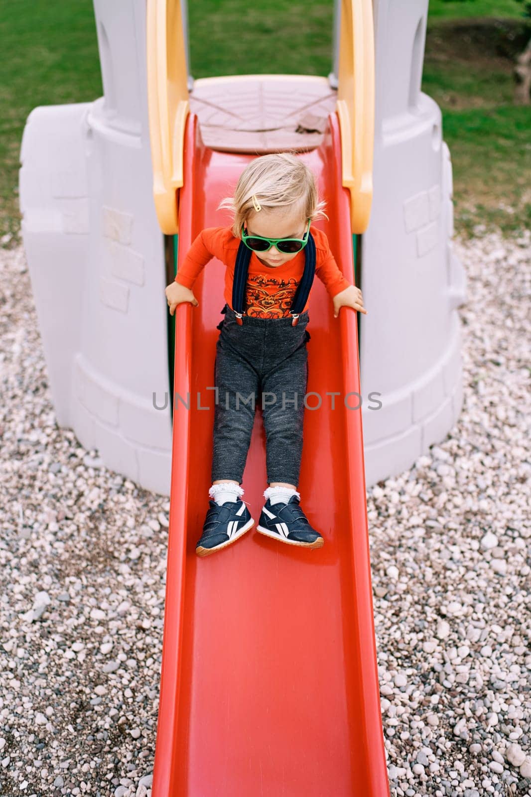Little girl slides down a slide holding on to the handrails. High quality photo