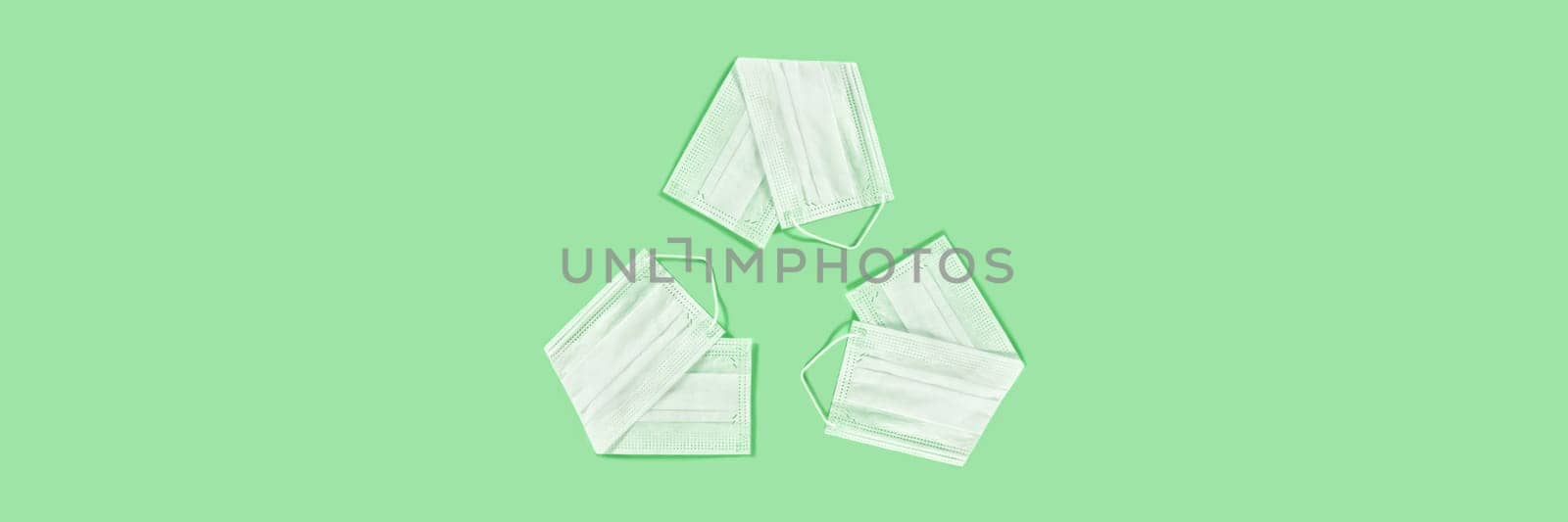 The universal recycling symbol made from the medical masks on green background.