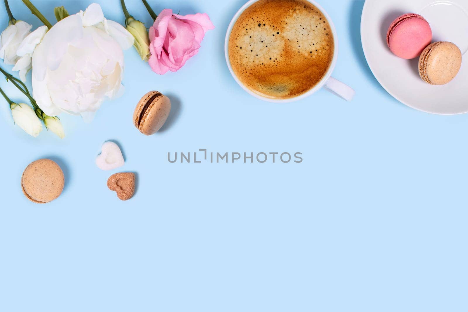Blue background with cup of tasty coffee, macaroons, peonies and roses. Top view with space for your text.