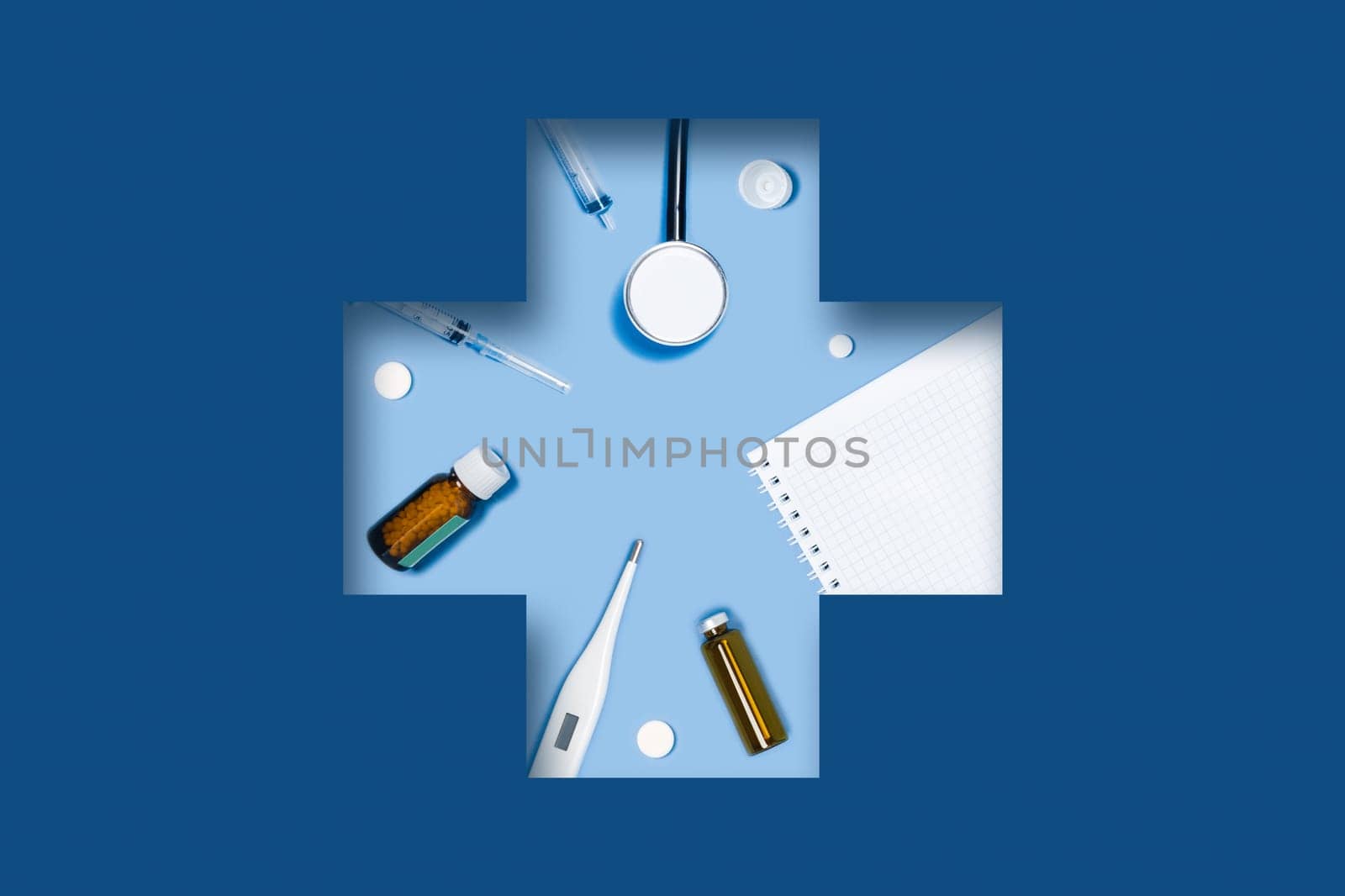 Medical classic blue background with accessories: syringe, tablets, thermometer, stethoscope, Notepad, ampoule lying in a carved medical cross.