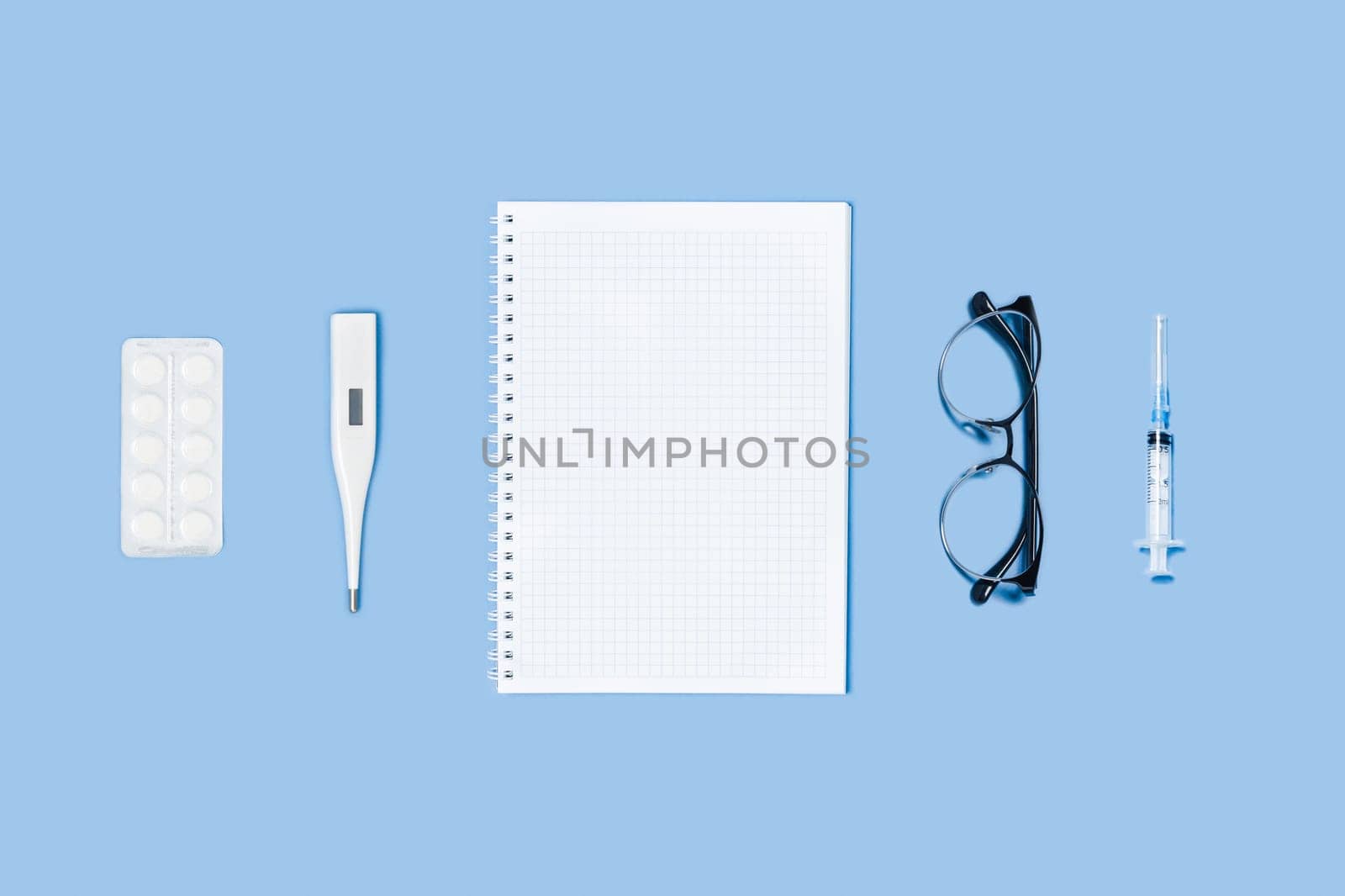 Medical blue background with different accessories: notepad, syringe, thermometer, glasses and tablets.
