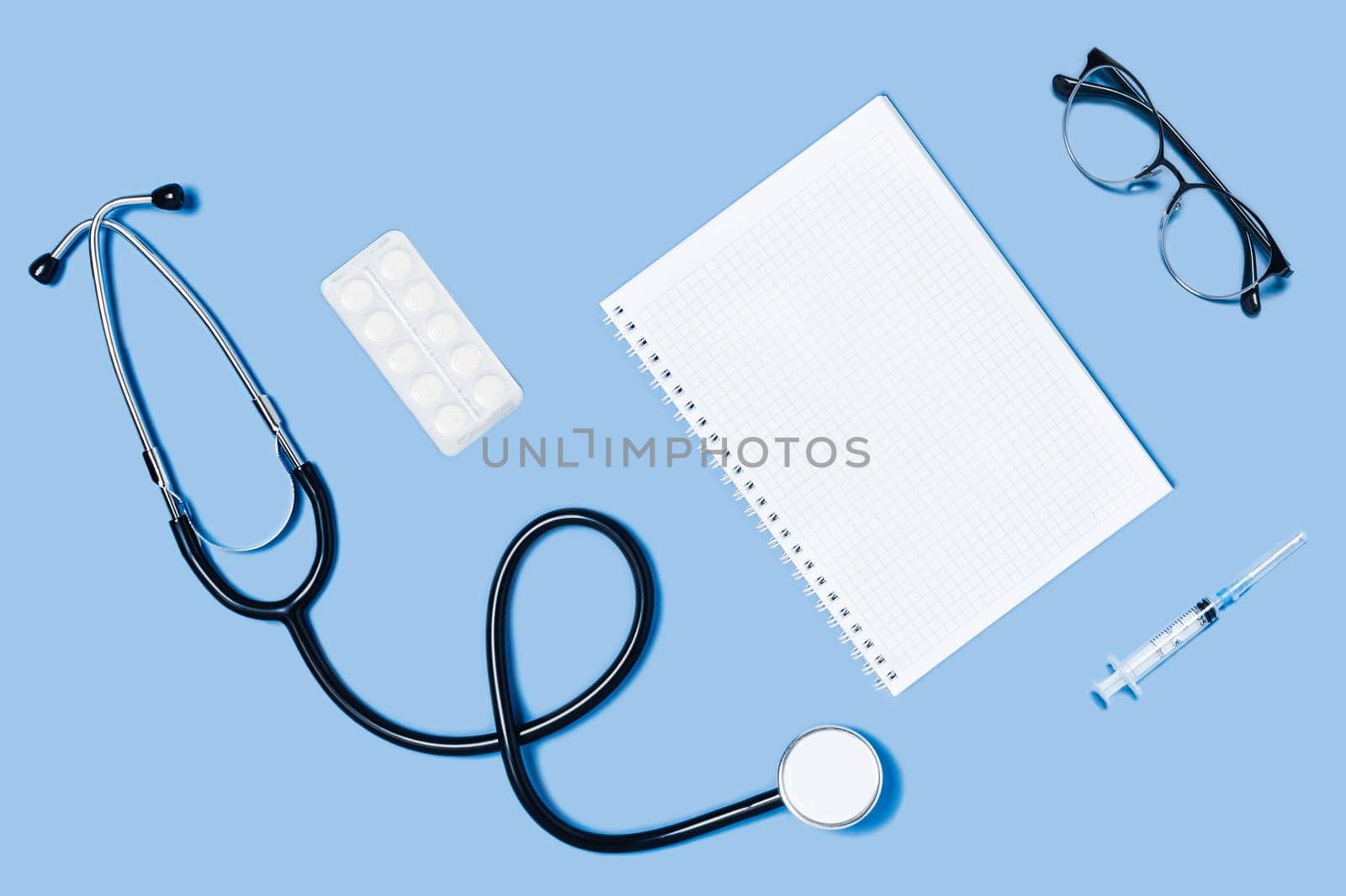 Medical blue background with different accessories: stethoscope, syringe notepad and glasses.