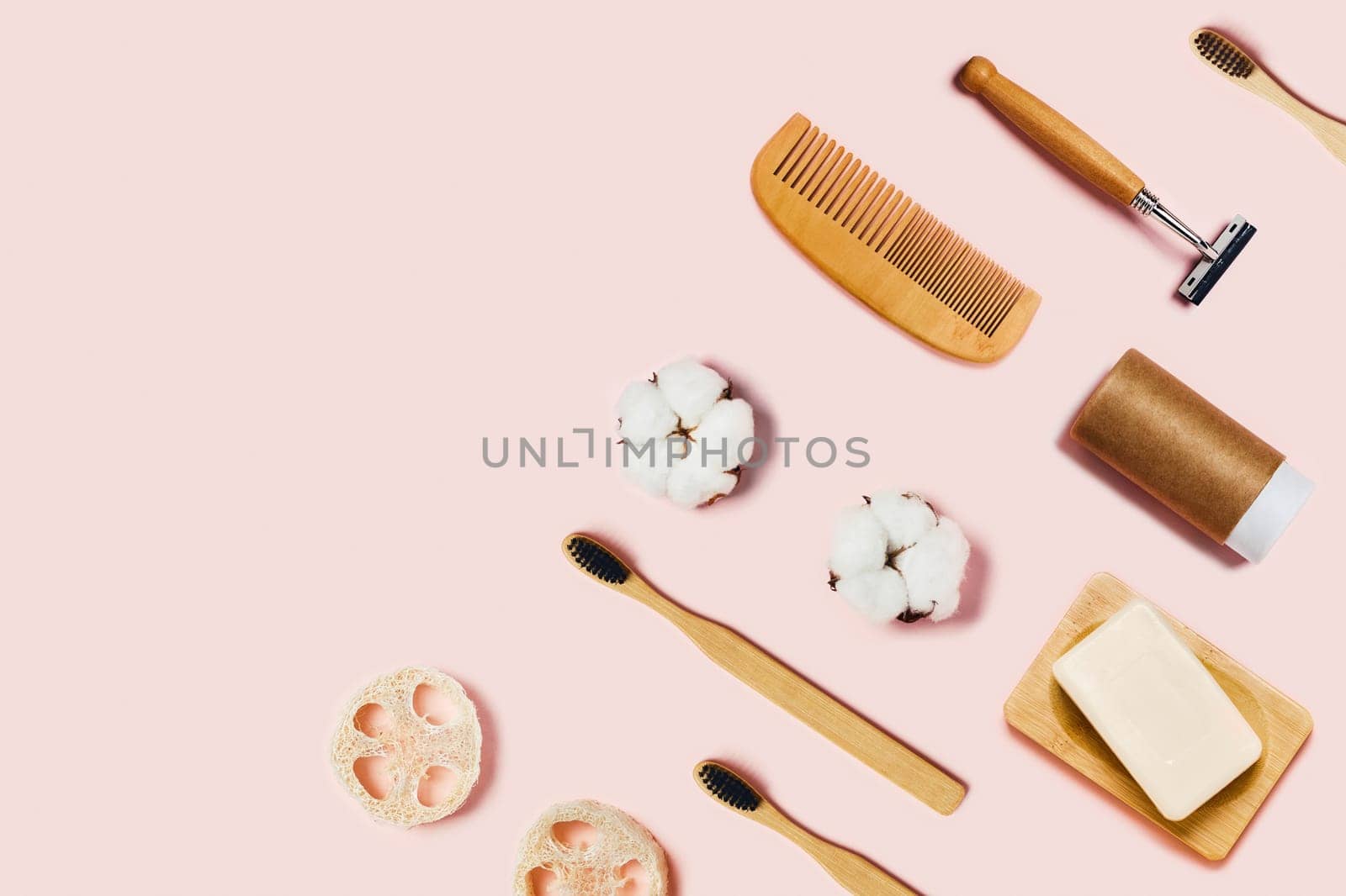 Bathroom accessories on pink background. Natural bamboo toothbrushes, sponges, cotton flowers, shaving brush and soap. Flat lay, top view.