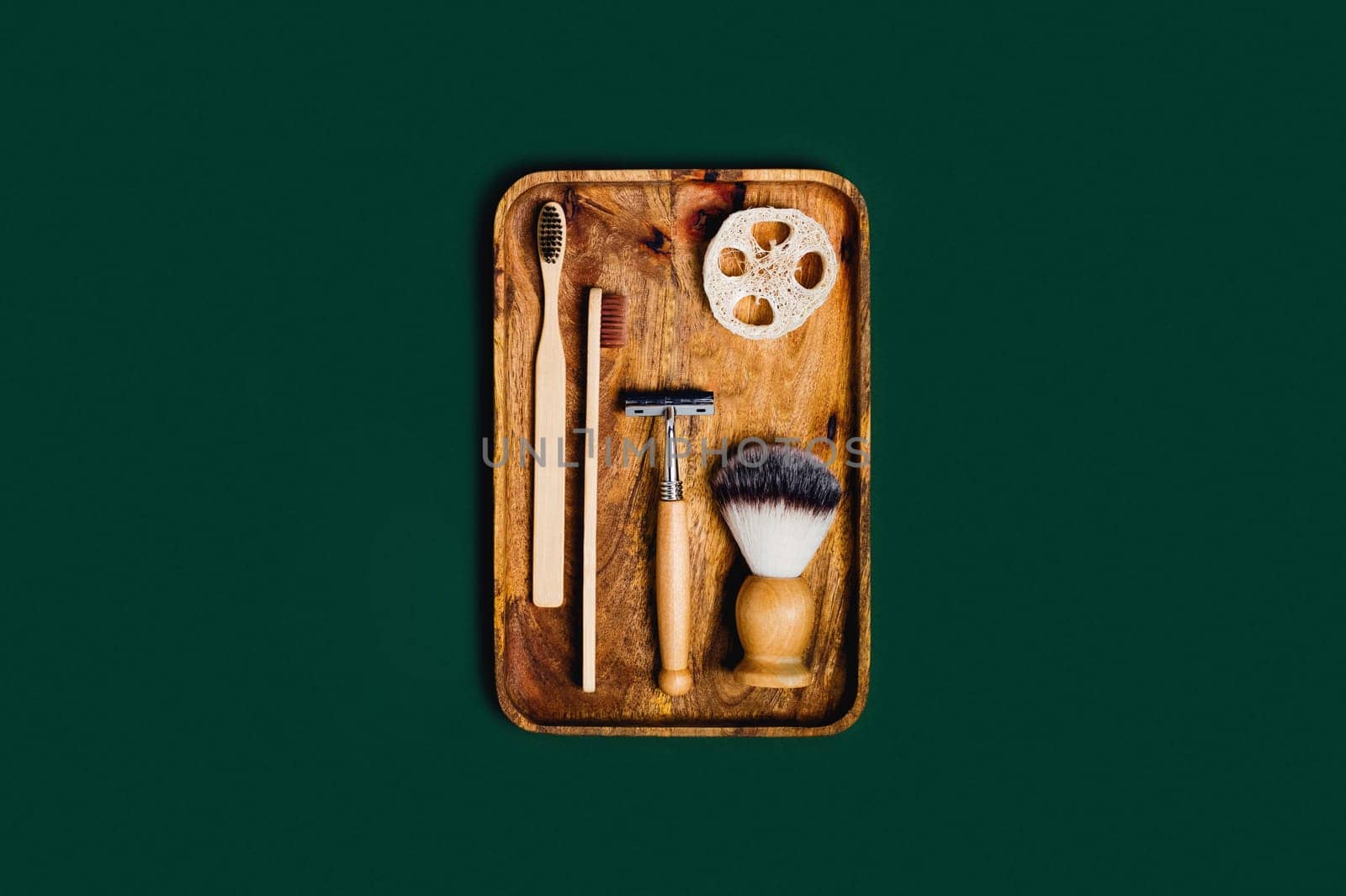 Zero waste concept. Natural bamboo toothbrushes , razor, natural sponge, shaving brush located on wooden tray on green background.