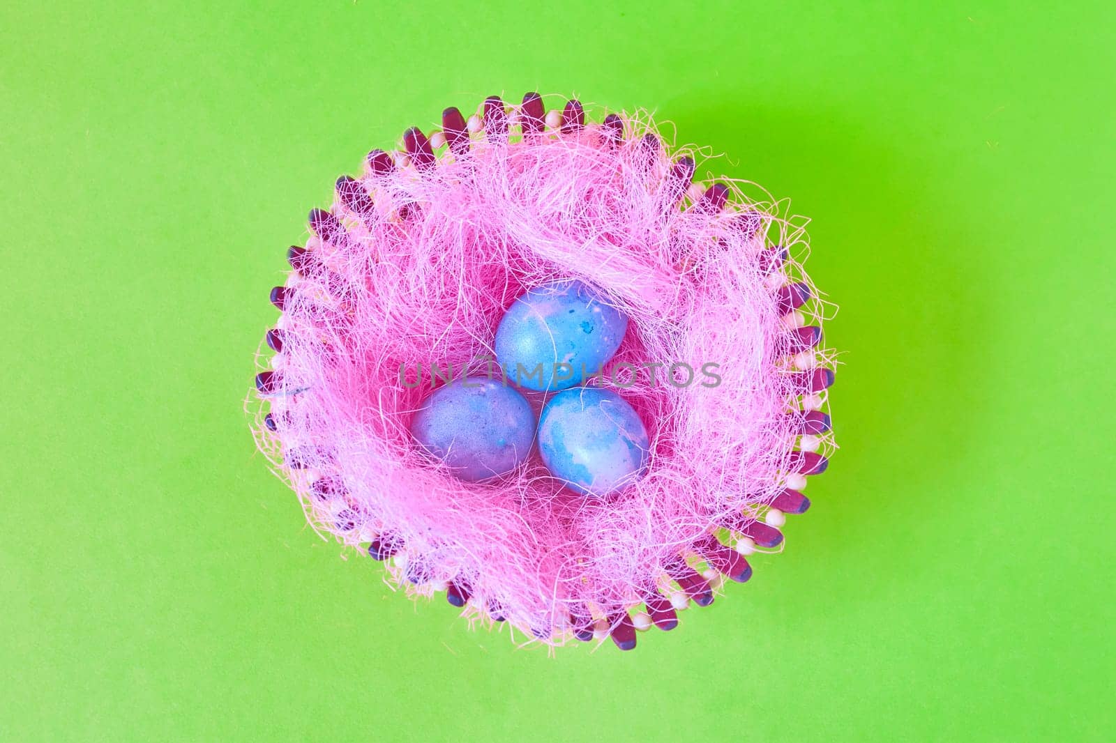 Three Easter eggs with space galactic pattern in a basket with a filler in the form of a pink nest on a green background. flat lay