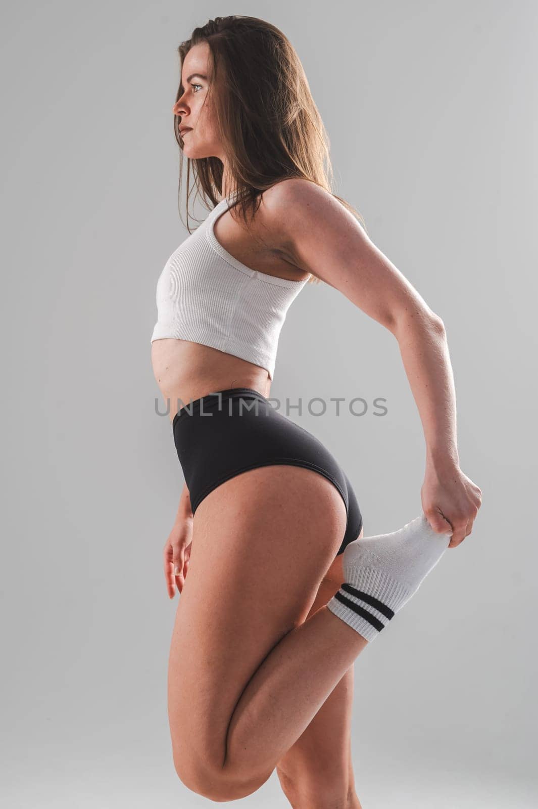 Athletic Caucasian woman stretching her quadriceps on a white background. Vertical photo