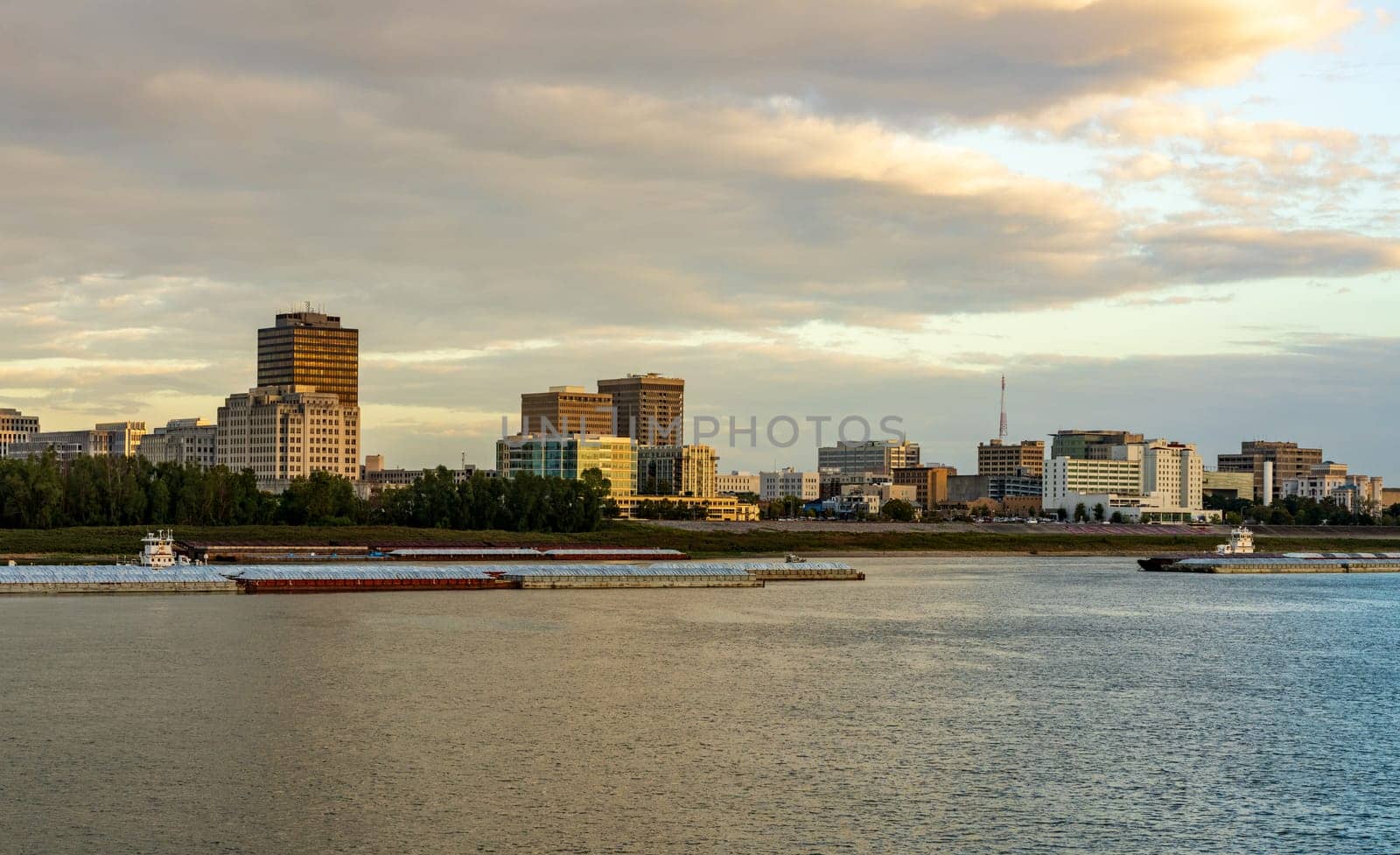 Skyline of Baton Rouge at sunset over river barges by steheap