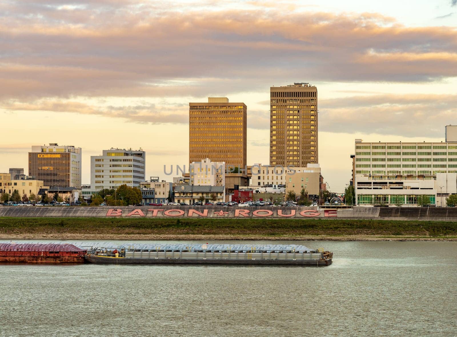 Skyline of Baton Rouge at sunset over river barges by steheap