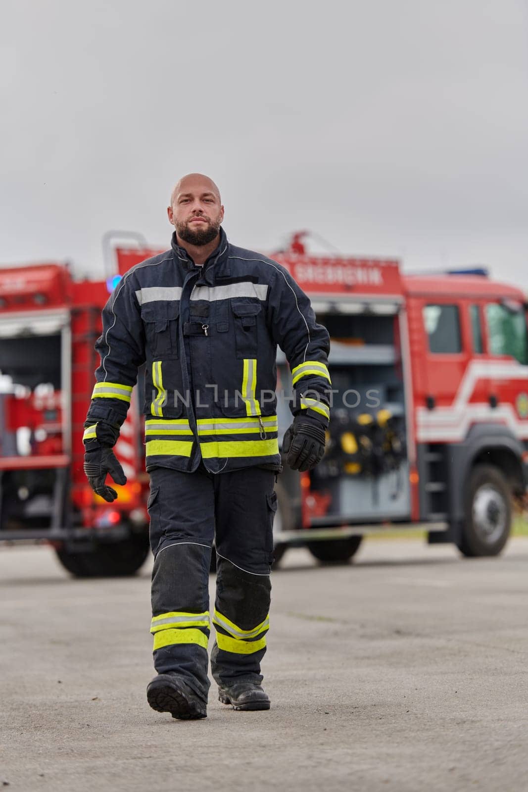 A symbolically brave firefighter strides forward with unwavering courage, epitomizing dedication and leadership, while behind him, a modern firetruck stands ready for firefighting actions, capturing the essence of heroism and preparedness in the face of emergency by dotshock