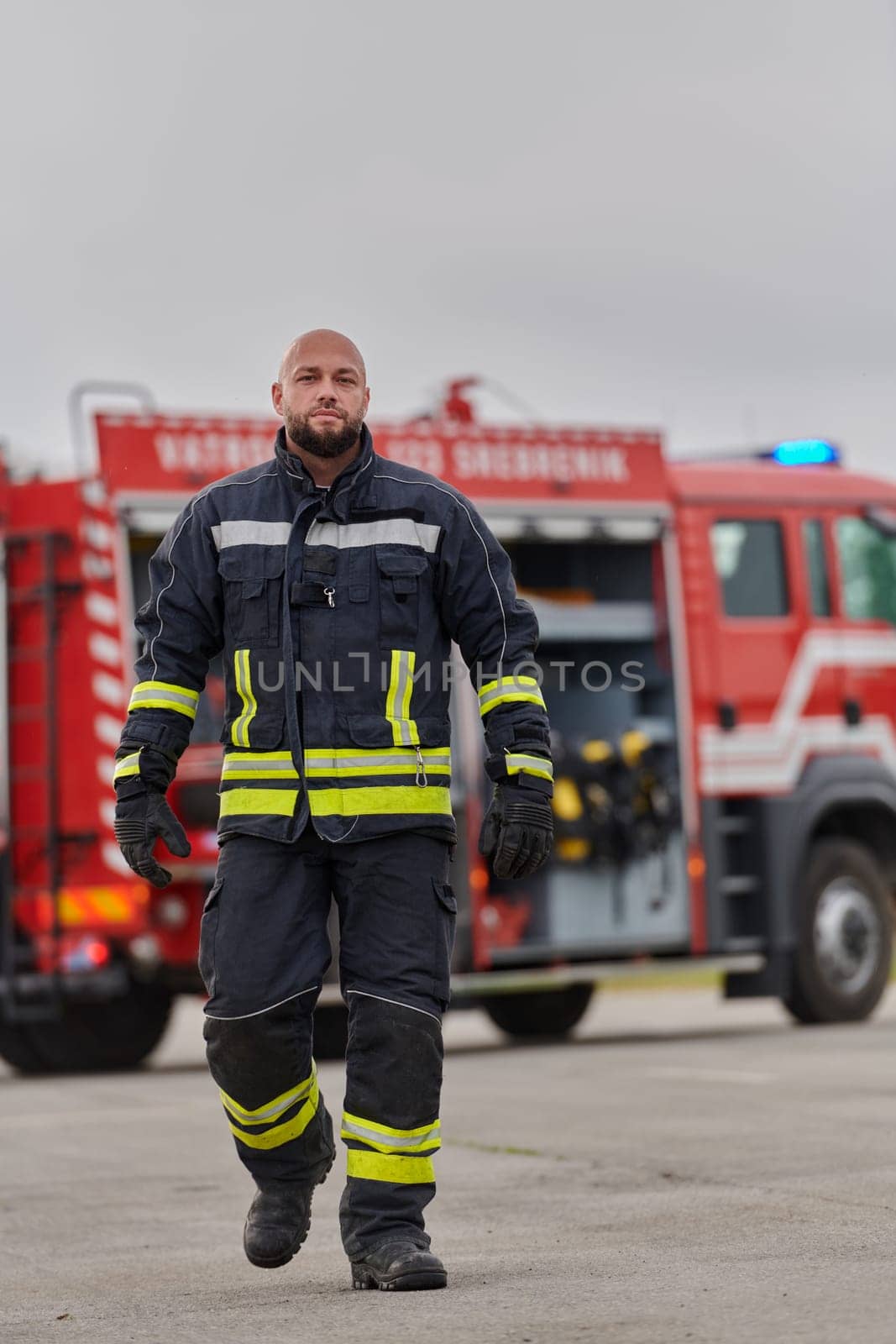 A symbolically brave firefighter strides forward with unwavering courage, epitomizing dedication and leadership, while behind him, a modern firetruck stands ready for firefighting actions, capturing the essence of heroism and preparedness in the face of emergency.