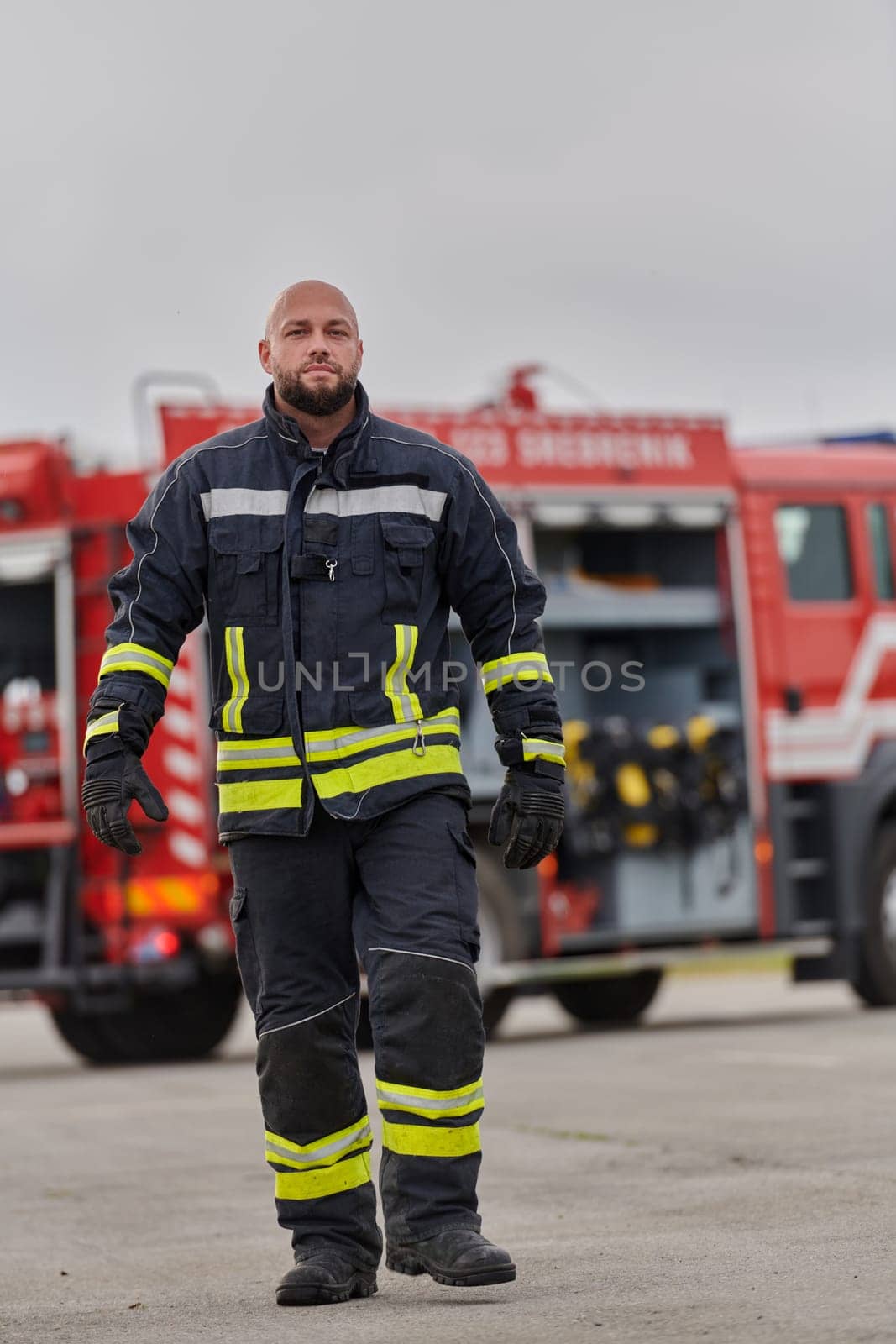 A symbolically brave firefighter strides forward with unwavering courage, epitomizing dedication and leadership, while behind him, a modern firetruck stands ready for firefighting actions, capturing the essence of heroism and preparedness in the face of emergency.