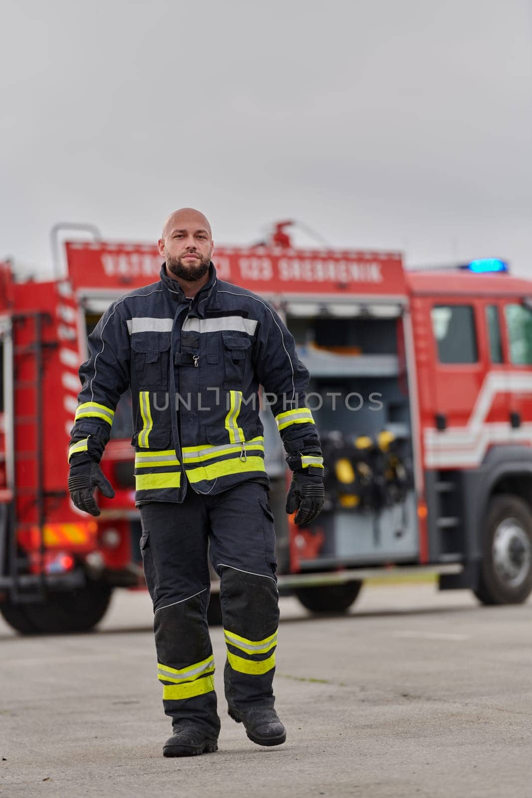 A symbolically brave firefighter strides forward with unwavering courage, epitomizing dedication and leadership, while behind him, a modern firetruck stands ready for firefighting actions, capturing the essence of heroism and preparedness in the face of emergency by dotshock