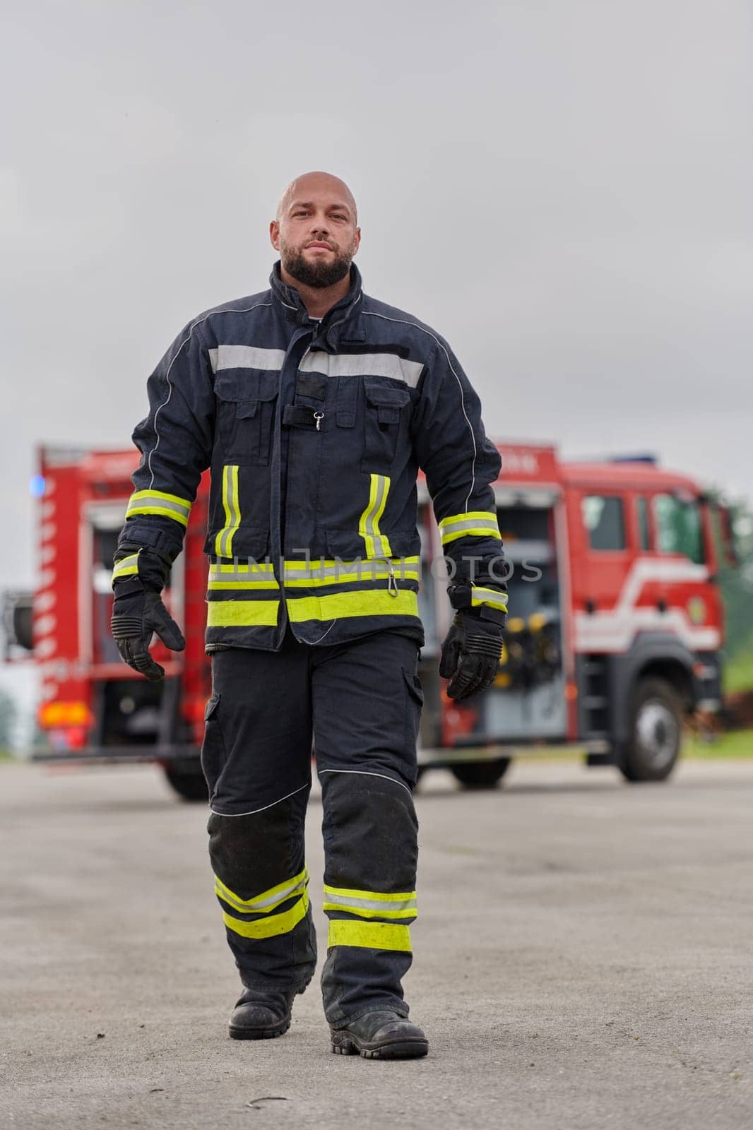 A symbolically brave firefighter strides forward with unwavering courage, epitomizing dedication and leadership, while behind him, a modern firetruck stands ready for firefighting actions, capturing the essence of heroism and preparedness in the face of emergency.