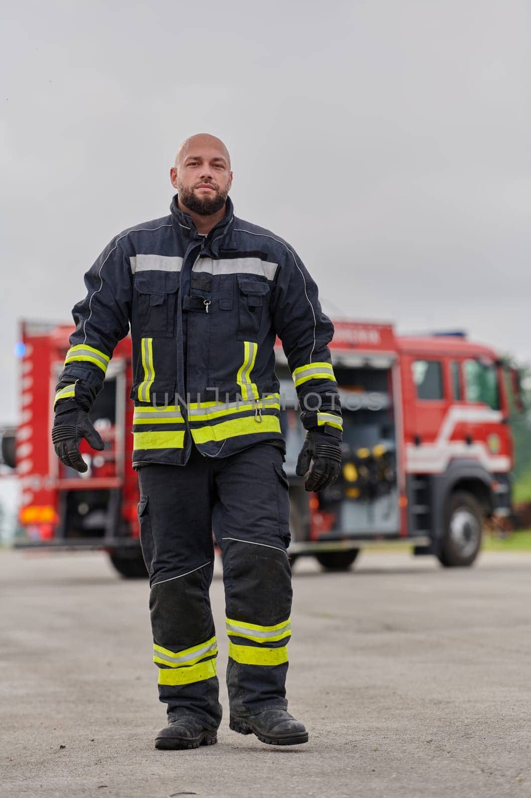 A symbolically brave firefighter strides forward with unwavering courage, epitomizing dedication and leadership, while behind him, a modern firetruck stands ready for firefighting actions, capturing the essence of heroism and preparedness in the face of emergency.