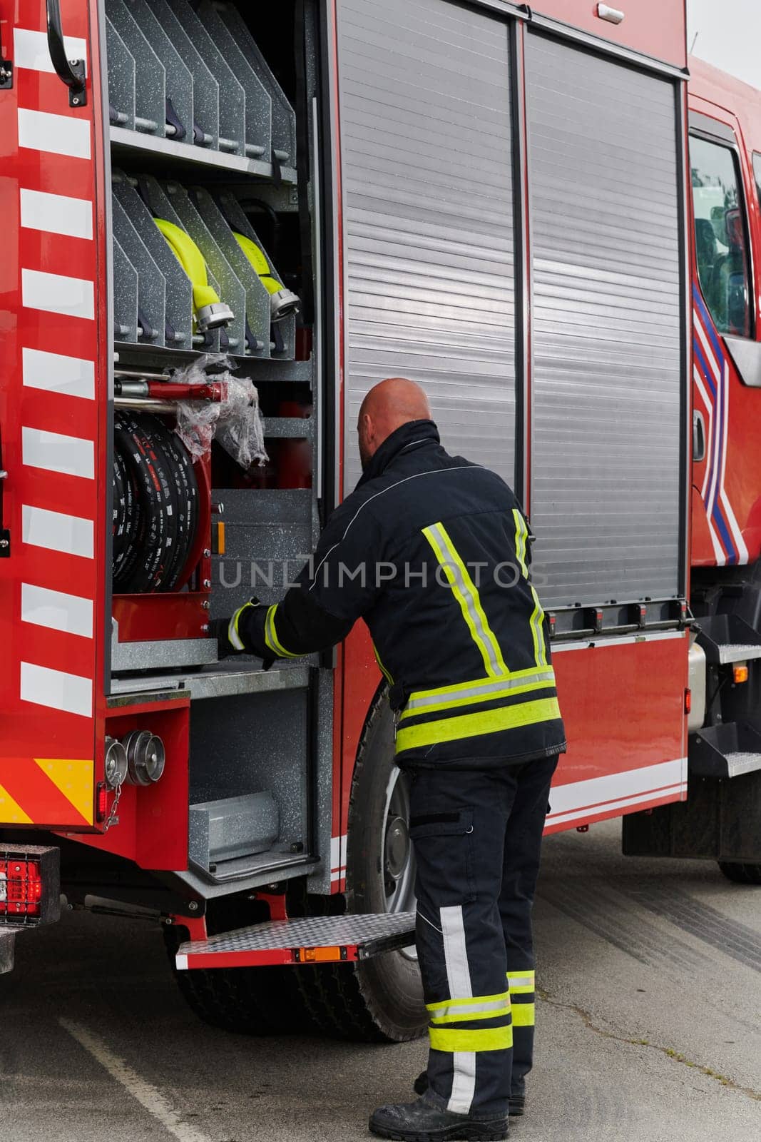 A firefighter meticulously prepares a modern firetruck for a mission to evacuate and respond to dangerous situations, showcasing the utmost dedication to safety and readiness in the face of a fire emergency by dotshock