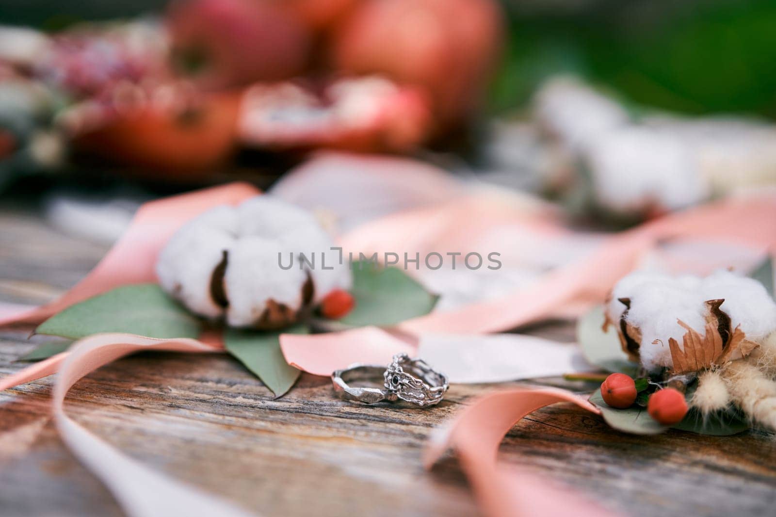 Wedding rings lie on a wooden table near ribbons and cotton flowers by Nadtochiy