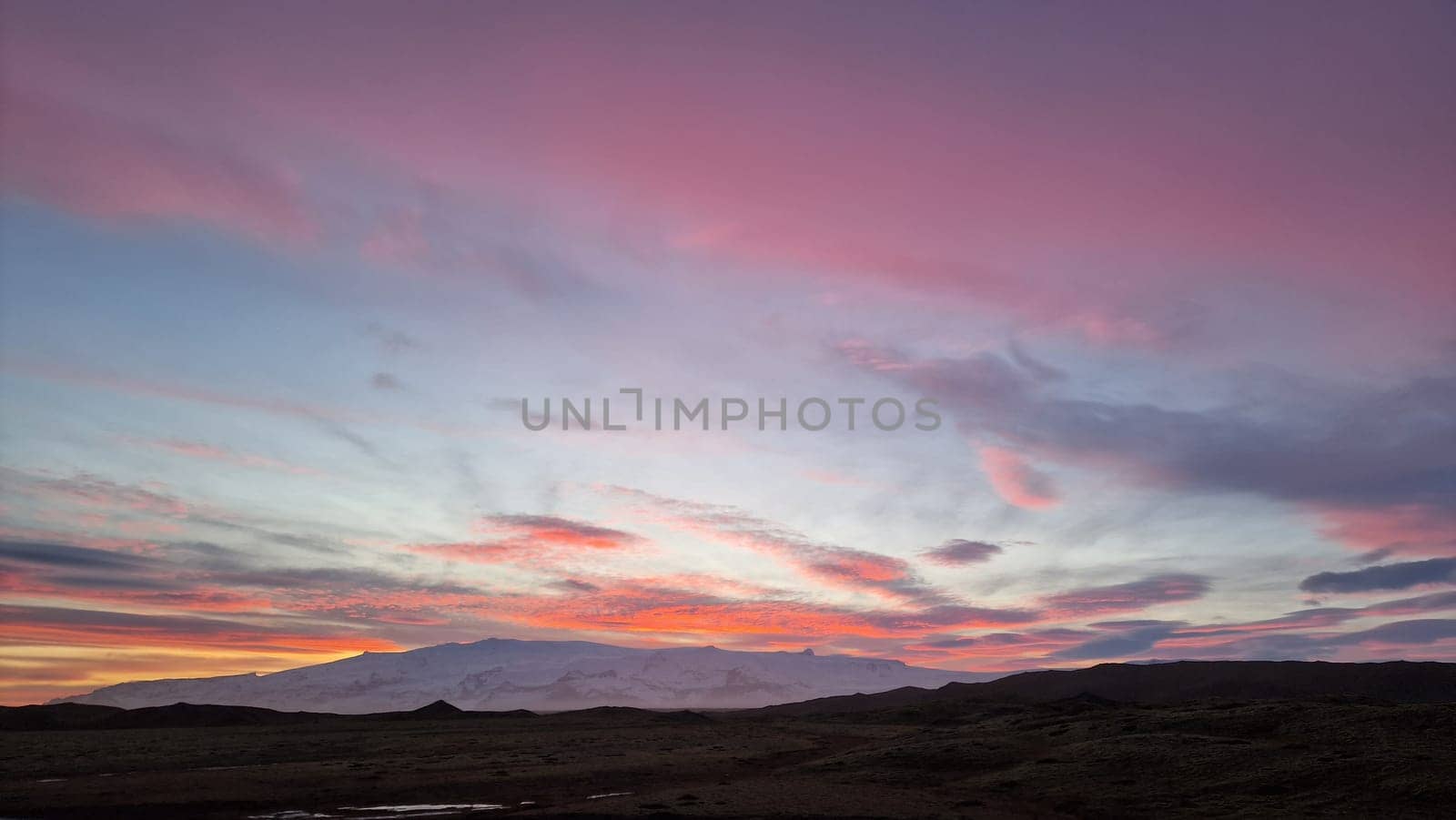Icelandic nordic colored sky at sunset, beautiful pink and yellow clouds painting magical nordic scenery. Majestic scandinavian view of rosy cotton candy light due to sun setting above mountain.