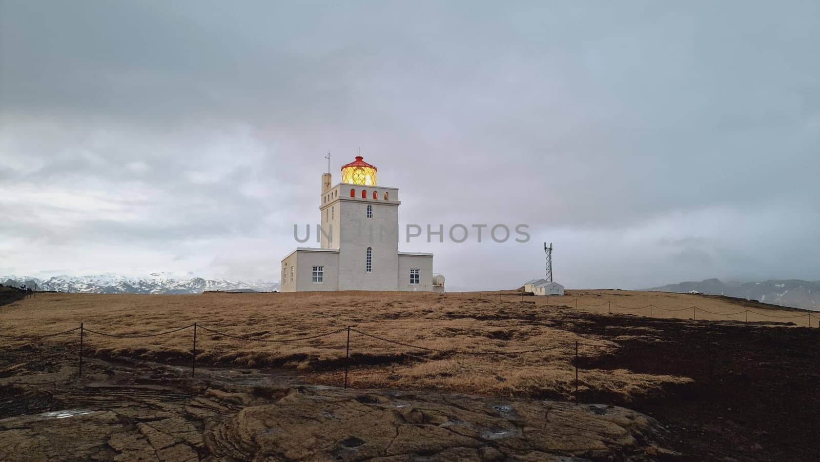 Dyrholaey beautiful lighthouse on icelandic peninsula with frozen fields and guidance building near ocean coastline. Amazing colorful tower used for navigation as beacon of light in iceland.