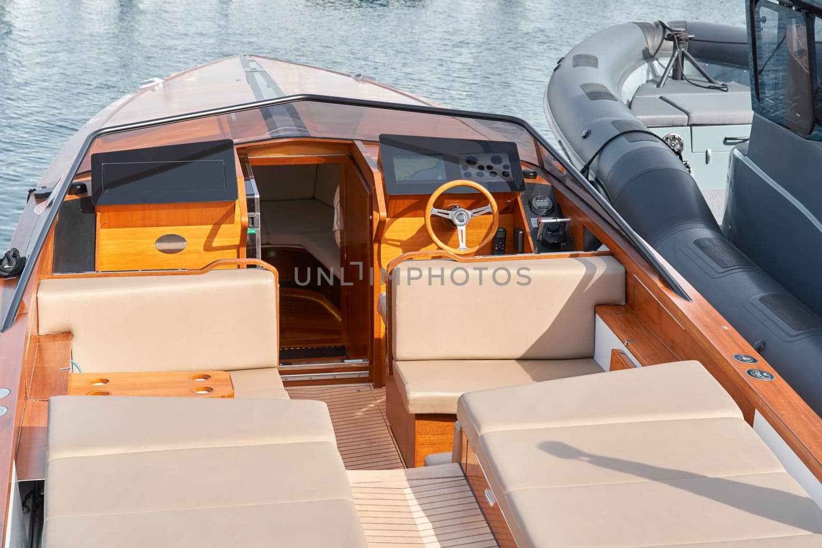 Close-up view of a relaxation area on the open teak deck of an expensive motorboat at sunny day, Monaco yacht show, large boat exhibition, wealth life, table and chairs by vladimirdrozdin